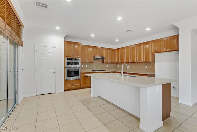 kitchen featuring an island with sink, stainless steel appliances, ornamental molding, light tile patterned flooring, and sink