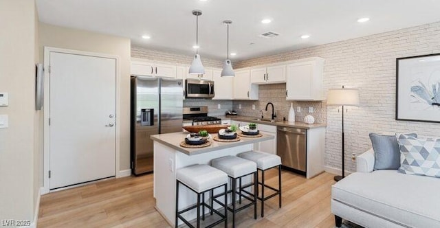 kitchen featuring stainless steel appliances, a kitchen island, pendant lighting, light hardwood / wood-style floors, and white cabinetry