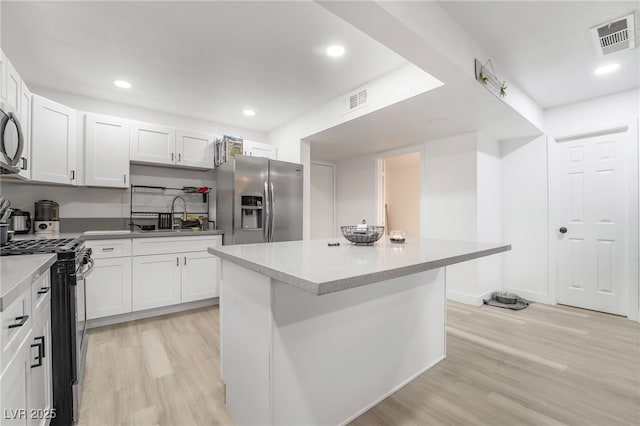 kitchen with white cabinets, appliances with stainless steel finishes, a kitchen island, light hardwood / wood-style floors, and sink