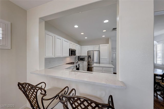 kitchen featuring appliances with stainless steel finishes, a kitchen breakfast bar, tasteful backsplash, white cabinets, and kitchen peninsula