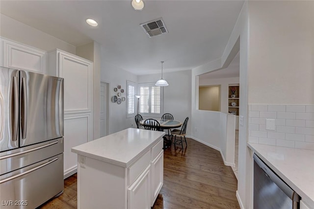 kitchen with stainless steel refrigerator, white cabinets, a kitchen island, dark hardwood / wood-style flooring, and decorative light fixtures