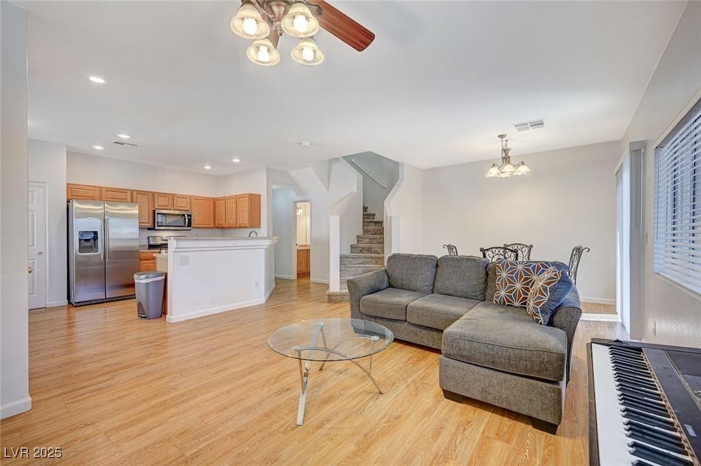 living room featuring ceiling fan with notable chandelier and light hardwood / wood-style flooring