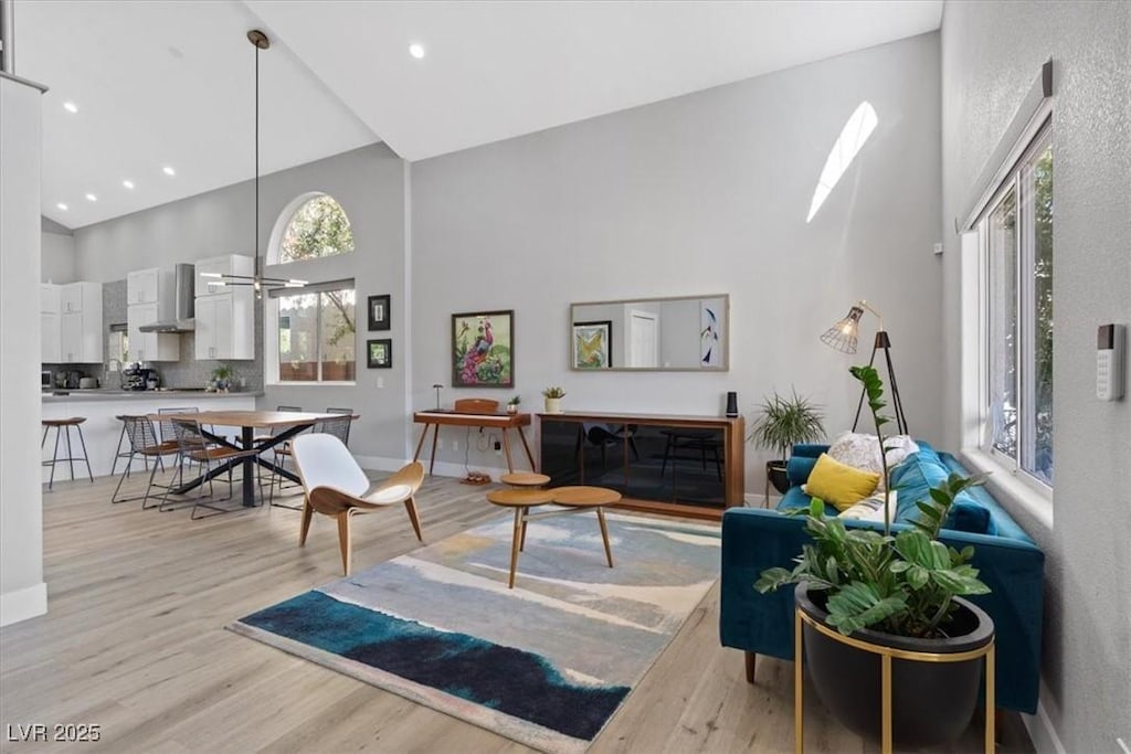 living room with a wealth of natural light, high vaulted ceiling, and light wood-type flooring