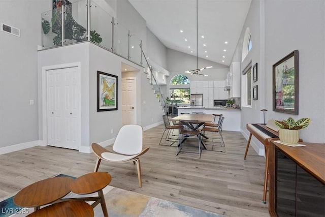 dining area featuring a towering ceiling, a notable chandelier, and light wood-type flooring