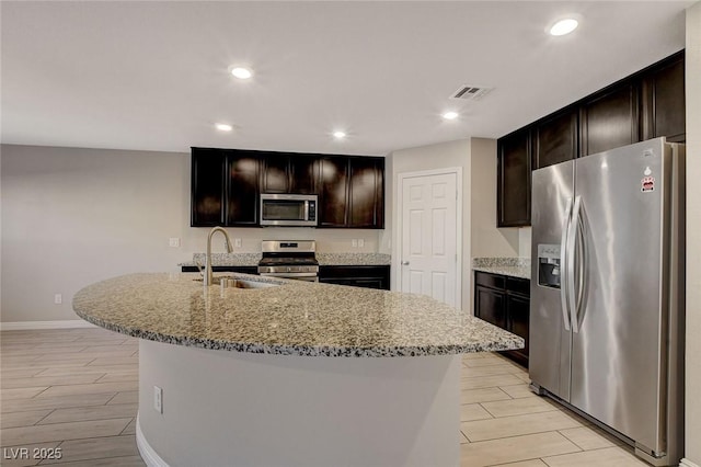 kitchen featuring light stone countertops, sink, appliances with stainless steel finishes, and an island with sink