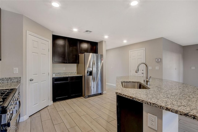 kitchen featuring light stone countertops, sink, a kitchen island with sink, appliances with stainless steel finishes, and light wood-type flooring