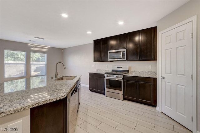 kitchen featuring light stone countertops, sink, dark brown cabinets, appliances with stainless steel finishes, and light wood-type flooring