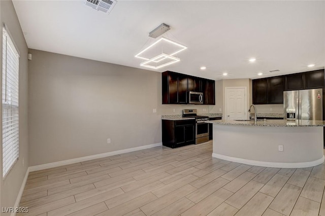 kitchen with light stone counters, dark brown cabinets, stainless steel appliances, sink, and light hardwood / wood-style flooring