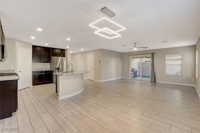 kitchen featuring light stone countertops, stainless steel appliances, a center island with sink, and ceiling fan