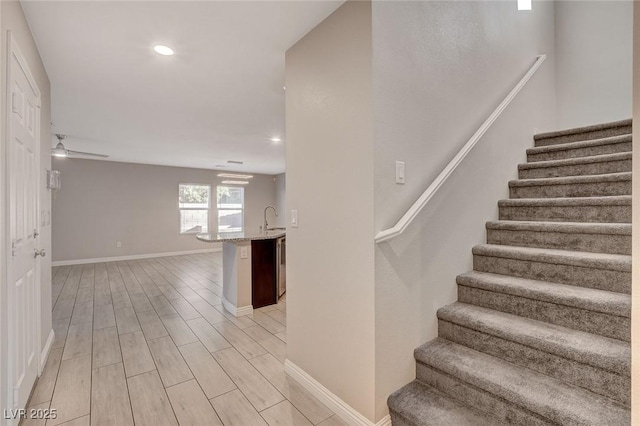 staircase featuring ceiling fan, sink, and wood-type flooring