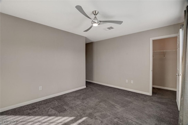 unfurnished bedroom with dark colored carpet, ceiling fan, a spacious closet, and a closet