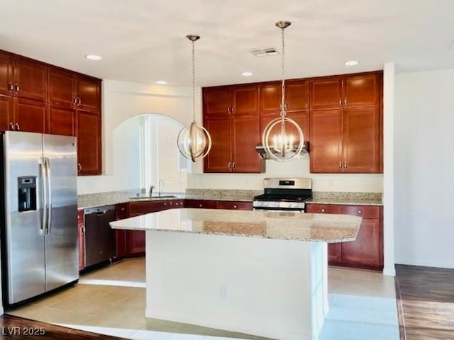 kitchen with sink, light stone counters, decorative light fixtures, a kitchen island, and appliances with stainless steel finishes