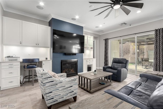 living room featuring ceiling fan, a large fireplace, light wood-type flooring, and crown molding