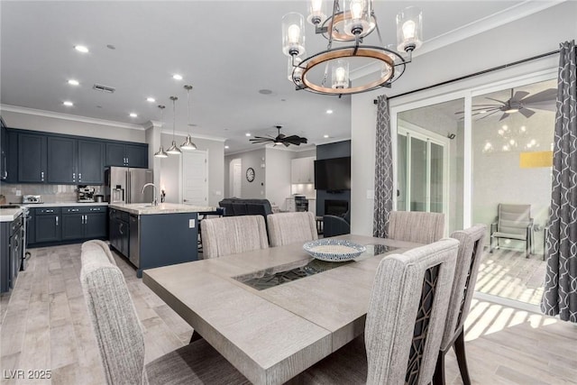 dining space featuring ceiling fan with notable chandelier, sink, crown molding, and light hardwood / wood-style flooring