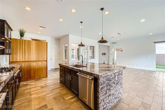 kitchen featuring pendant lighting, dishwasher, an island with sink, sink, and dark stone counters