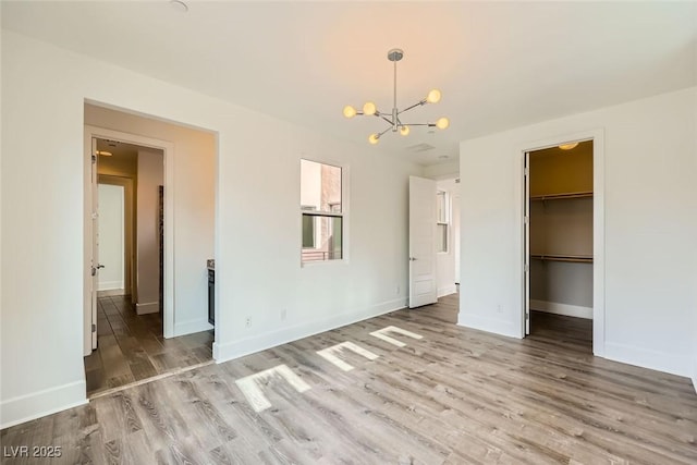 unfurnished bedroom with a spacious closet, a chandelier, a closet, and light wood-type flooring