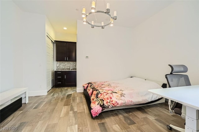 bedroom with sink, an inviting chandelier, and light wood-type flooring