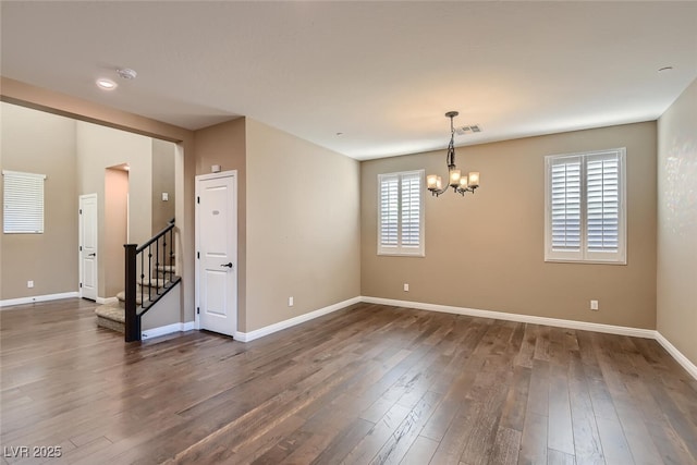 spare room with a healthy amount of sunlight, dark wood-type flooring, and an inviting chandelier