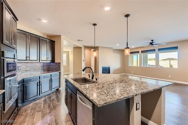 kitchen with dark brown cabinetry, sink, stainless steel dishwasher, pendant lighting, and a center island with sink