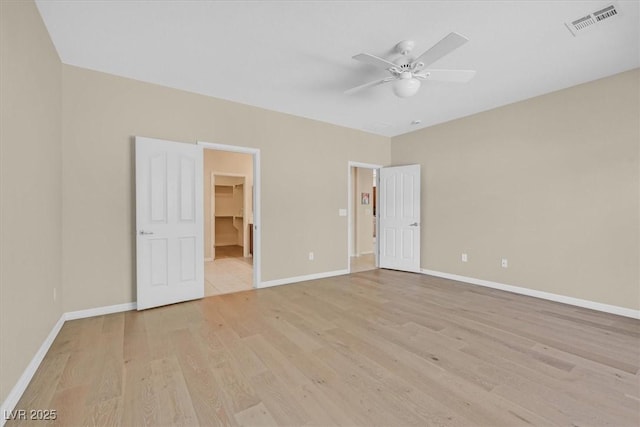 unfurnished bedroom featuring a walk in closet, a closet, light hardwood / wood-style flooring, and ceiling fan