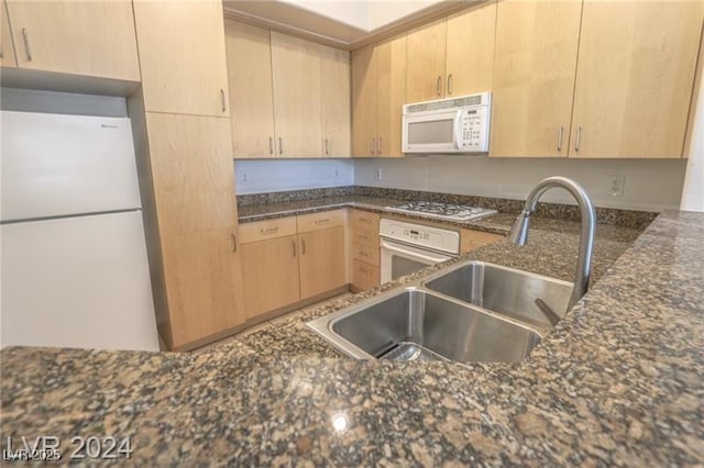 kitchen with dark stone countertops, white appliances, sink, and light brown cabinetry