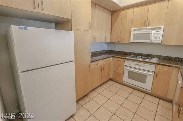 kitchen with light brown cabinets, white appliances, light tile patterned floors, and dark stone counters