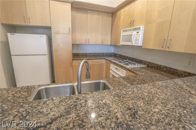 kitchen with light brown cabinets, white appliances, dark stone counters, and sink