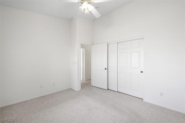 unfurnished bedroom featuring ceiling fan, light colored carpet, a towering ceiling, and a closet