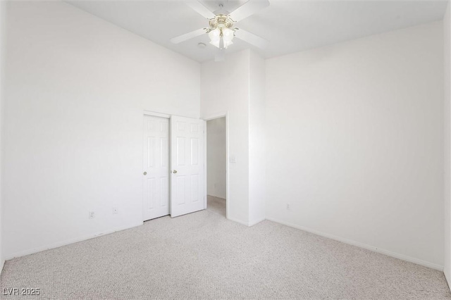 unfurnished room featuring ceiling fan, light colored carpet, and a high ceiling