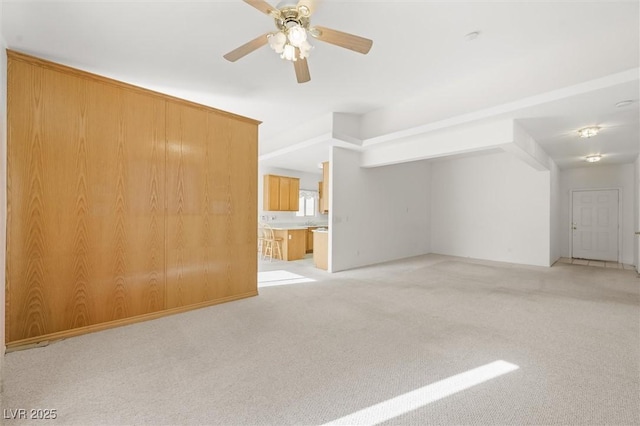 unfurnished living room with ceiling fan, light colored carpet, and wooden walls