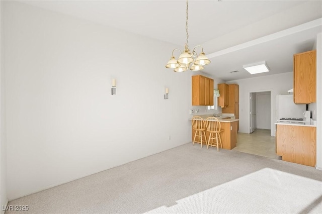 kitchen featuring kitchen peninsula, light carpet, decorative light fixtures, an inviting chandelier, and white fridge