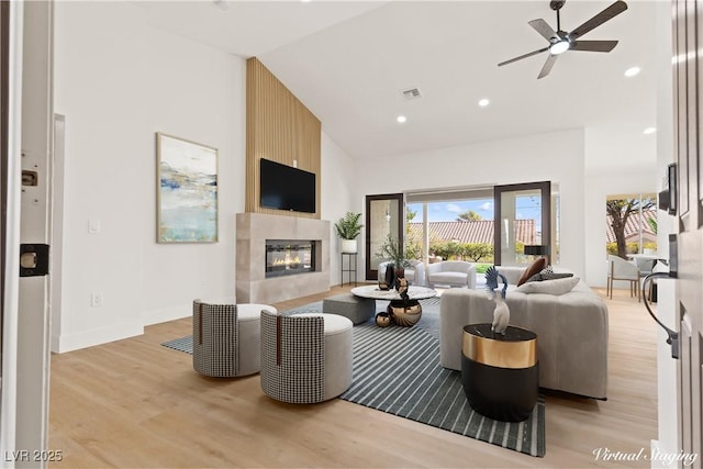 living room featuring light wood-type flooring, high vaulted ceiling, ceiling fan, and a tiled fireplace