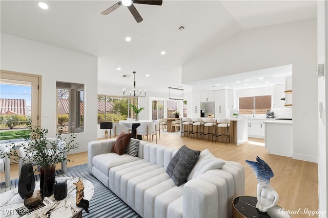 living room with light wood-type flooring, ceiling fan with notable chandelier, and lofted ceiling