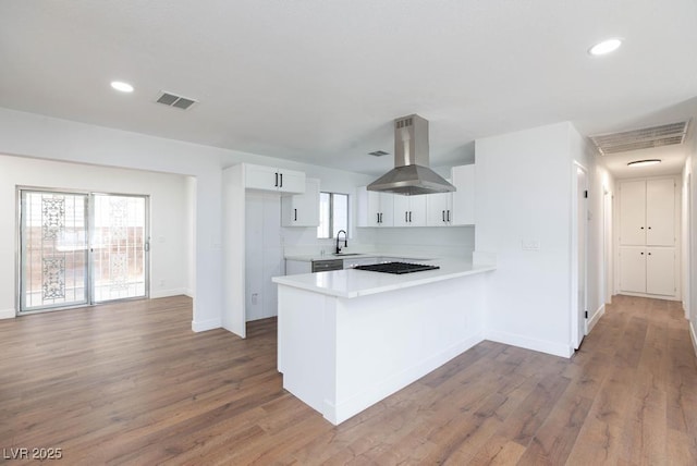 kitchen with kitchen peninsula, wall chimney exhaust hood, sink, hardwood / wood-style flooring, and white cabinets