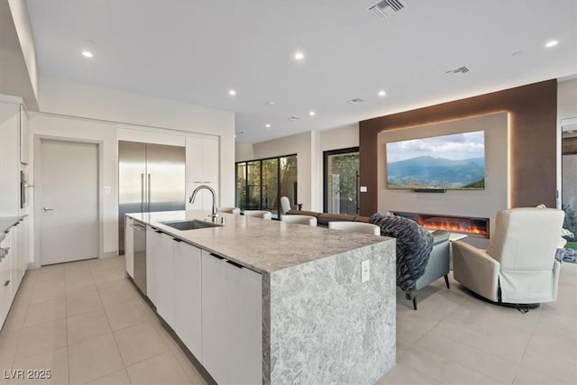 kitchen featuring a kitchen island with sink, a sink, visible vents, and white cabinets