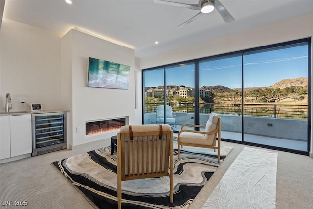 sitting room with beverage cooler, a glass covered fireplace, light colored carpet, a mountain view, and recessed lighting