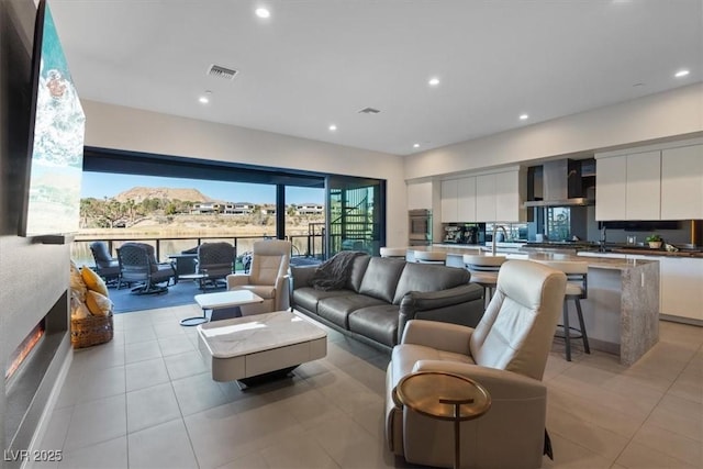 living area with light tile patterned floors, visible vents, a glass covered fireplace, and recessed lighting