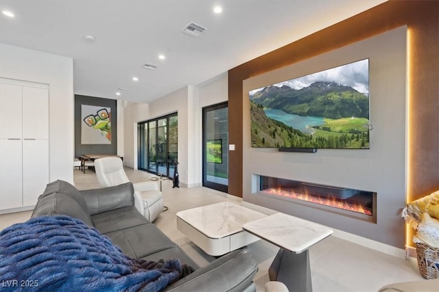 living room featuring baseboards, a glass covered fireplace, visible vents, and recessed lighting