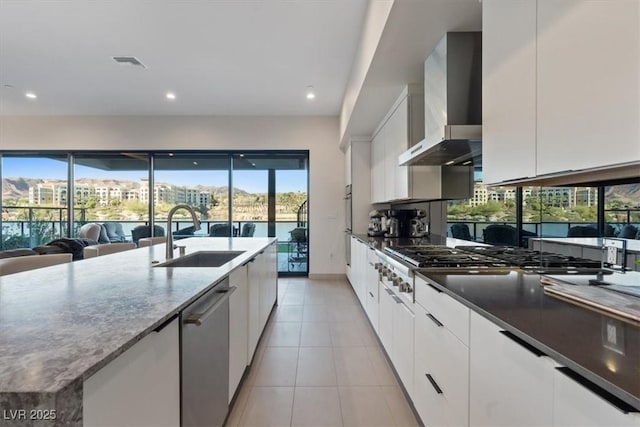 kitchen featuring stainless steel appliances, a sink, visible vents, white cabinetry, and wall chimney exhaust hood