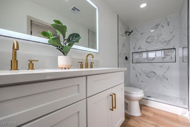 bathroom with vanity, toilet, wood-type flooring, and tiled shower