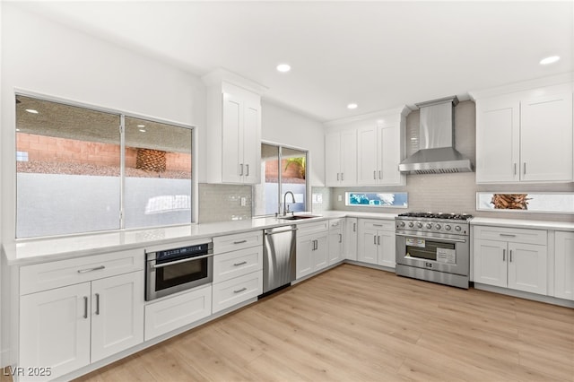 kitchen featuring white cabinets, sink, stainless steel appliances, and wall chimney range hood