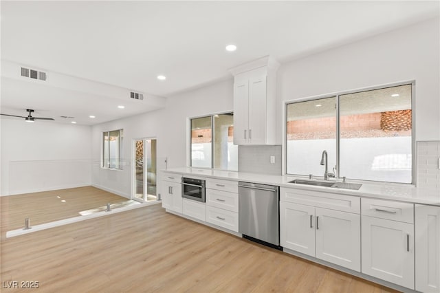 kitchen with appliances with stainless steel finishes, light wood-type flooring, tasteful backsplash, sink, and white cabinetry