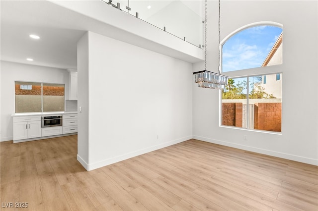 unfurnished living room with a chandelier, a high ceiling, and light wood-type flooring