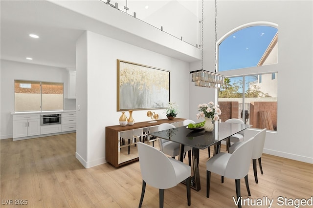 dining area with a notable chandelier, light hardwood / wood-style floors, and a high ceiling