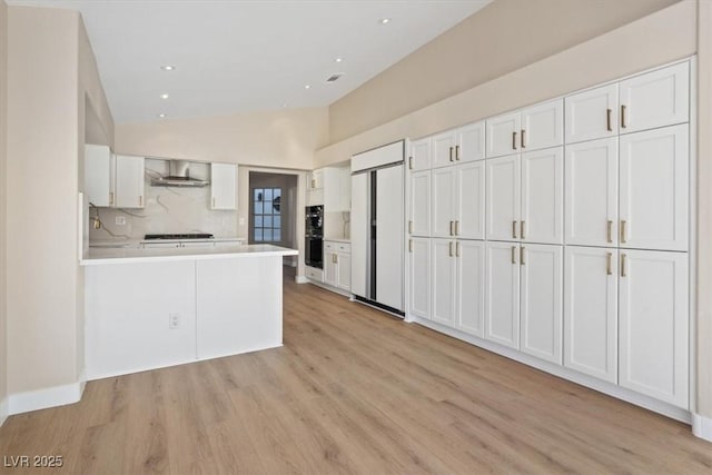 kitchen with kitchen peninsula, paneled refrigerator, wall chimney range hood, white cabinetry, and lofted ceiling