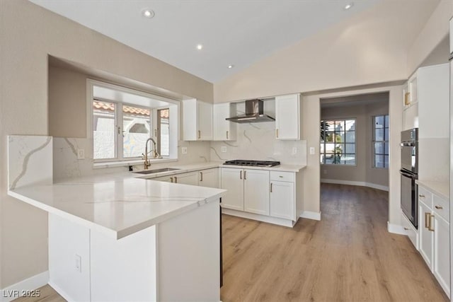 kitchen featuring white cabinets, lofted ceiling, sink, and wall chimney range hood