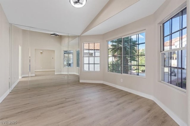 spare room featuring light wood-type flooring and vaulted ceiling