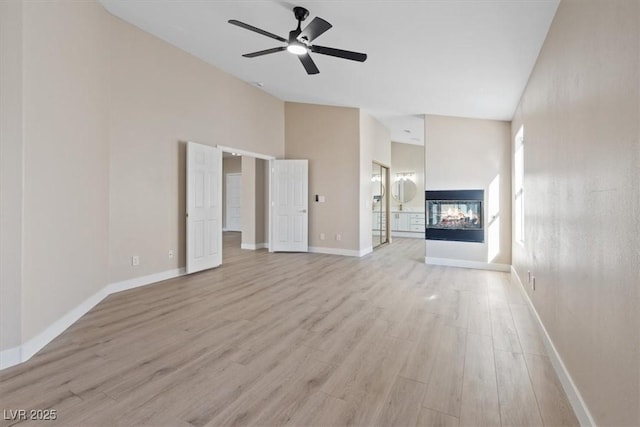 unfurnished living room with a multi sided fireplace, a towering ceiling, light hardwood / wood-style flooring, and ceiling fan