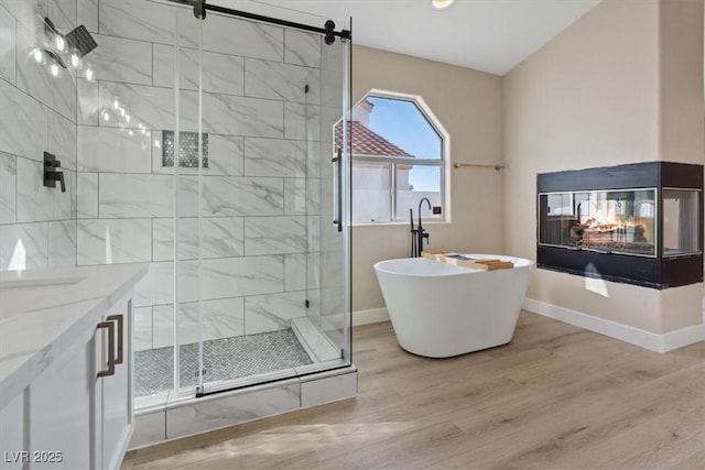 bathroom with a multi sided fireplace, hardwood / wood-style floors, vanity, and independent shower and bath