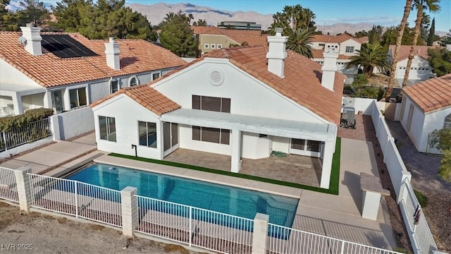 rear view of property featuring solar panels, a patio, and a fenced in pool